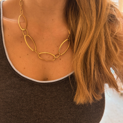 Colar dourado com elos ovais usados no pescoço de mulher com cabelo castanho claro
