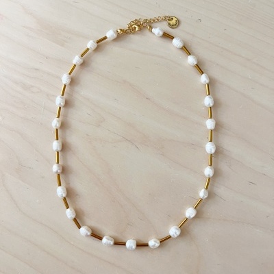 Colar branco com detalhes dourados sobre fundo de madeira clara