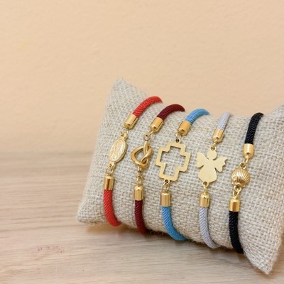 Pulseiras coloridas com pendentes dourados sobre almofada bege.