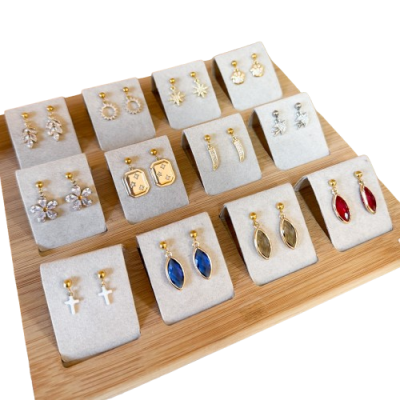 Doze pares de brincos variados em suportes bege sobre base de madeira