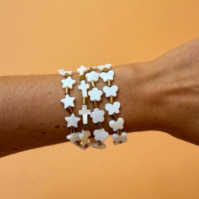 Pulseiras brancas de acrílico com formas de estrelas, cruzes e flores em pulso com fundo laranja