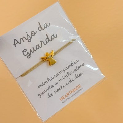 Pulseira com anjo dourado e cartão com texto em fundo bege