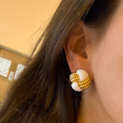 Brinco grande dourado e branco na orelha de mulher