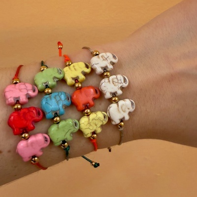 Pulseiras com elefantes coloridos e contas douradas no pulso sobre fundo laranja.