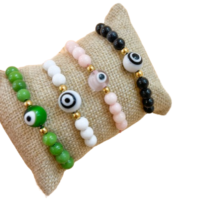 Conjunto de pulseiras coloridas com contas redondas e padrão de olho, exibidas numa almofada de tecido