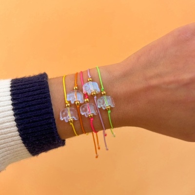 Pulseiras com pendente de elefante em cordão colorido numa mão com fundo laranja