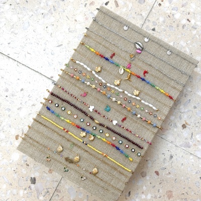 Pulseiras coloridas e metálicas exibidas em expositor têxtil sobre piso de pedra clara.
