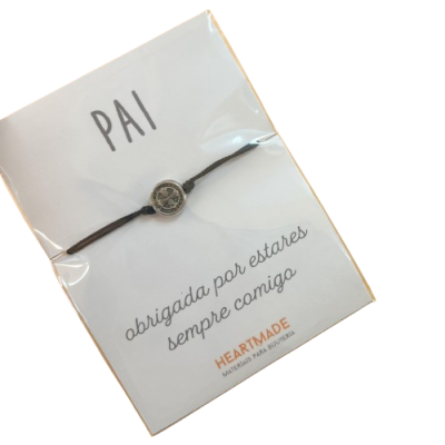 Pulseira com medalha prateada e cordão castanho em cartão branco com texto para Pai