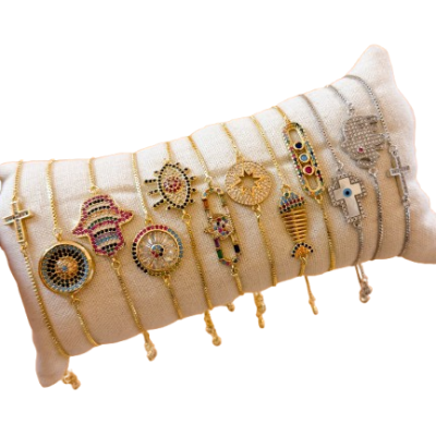 Pulseiras douradas e prateadas com pendentes variados em almofada bege