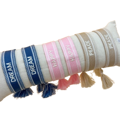 Braceletes têxteis coloridos com palavras bordadas e franjas em almofada bege