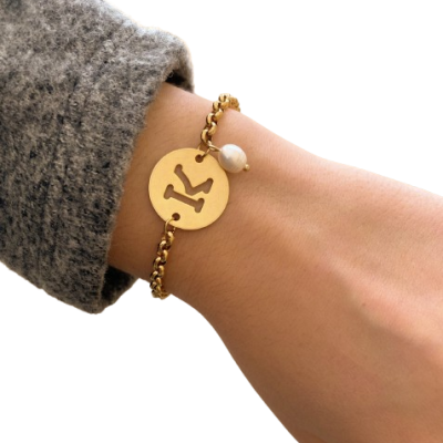 Pulseira dourada com medalha 'K' e pendente de pérola no pulso