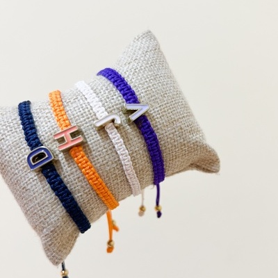 Pulseiras coloridas em fio trançado com letras metálicas num suporte almofadado