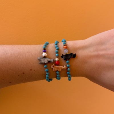 Pulseiras azuis com pingentes de animais no pulso contra fundo laranja