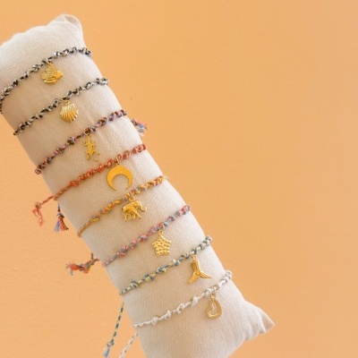 Pulseiras coloridas com pendentes dourados expostas num suporte de tecido bege