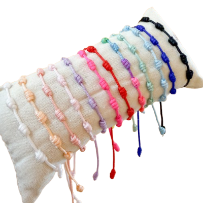 Pulseiras de cordão colorido com nós decorativos em almofada branca
