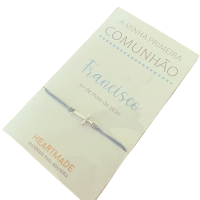 Pulseira com cruz em embalagem de cartão branco com texto em português.
