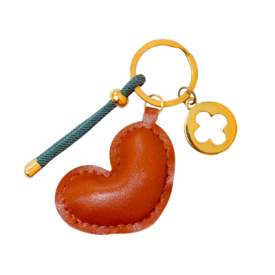 Porta-chaves com coração de couro castanho, corda verde e pendente metálico dourado em fundo branco