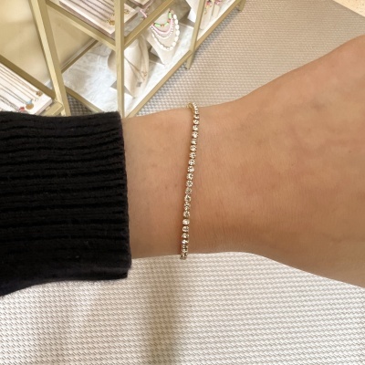 Pulseira fina dourada com pedras brilhantes no pulso