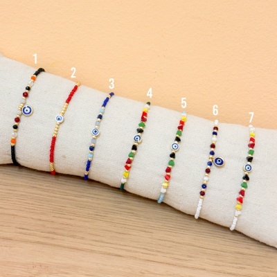 Sete pulseiras coloridas com pingente de olho grego em suporte de tecido bege