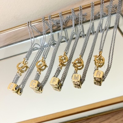 Conjunto de colares com pendentes em forma de cubo dourados com letras, correntes prateadas, sobre espelho com moldura dourada.