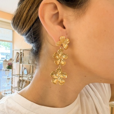 Brinco pendente dourado em forma de flores usadas numa orelha feminina