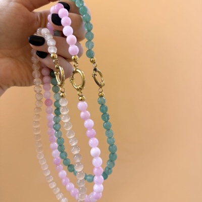 Pulseiras coloridas de contas com fechos dourados na mão de uma pessoa