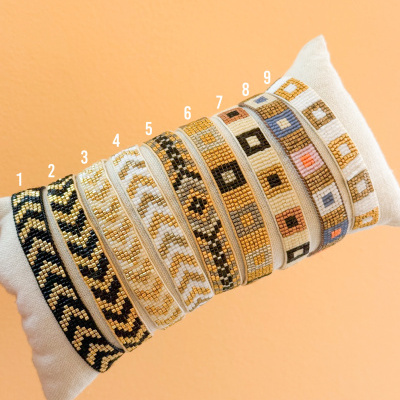 Oito pulseiras de contas coloridas em padrões geométricos sobre suporte de tecido creme