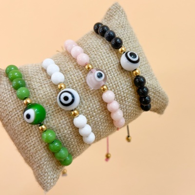 Pulseiras de contas em verde, branco, rosa e preto com padrão de olho central, sobre almofada de tecido rústico