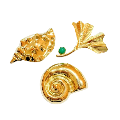 Três broches dourados em formas de concha, folha e caracol