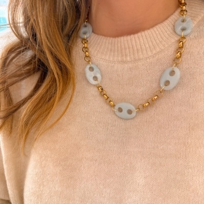 Colar dourado com peças ovais cinza claro numa camisola bege