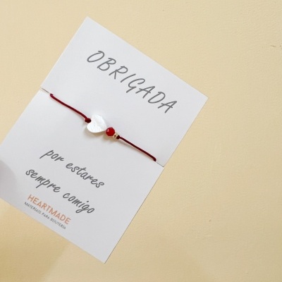 Pulseira com pendente de coração em cartão com mensagem e fundo bege