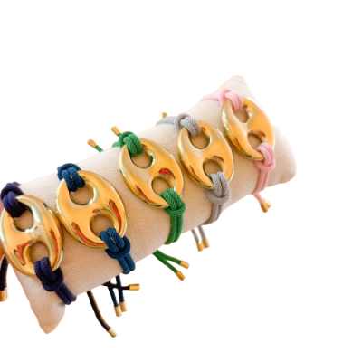 Pulseiras com elos dourados e cordões coloridos num suporte almofadado