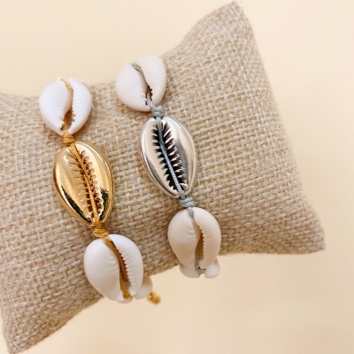 Pulseiras com búzios dourado e prateado sobre almofada de tecido natural
