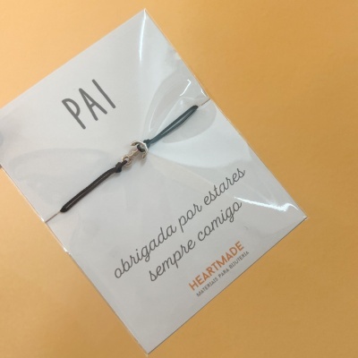 Pulseira preta em embalagem com cartão branco e texto em português para pai.