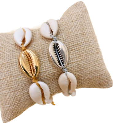 Duas pulseiras com conchas naturais e conchas metálicas dourada e prata sobre suporte de tecido bege.