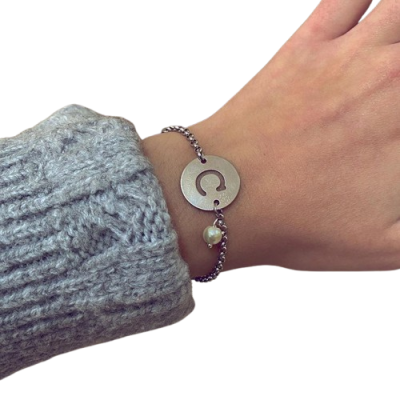 Pulseira de metal prateado com pendente redondo e pérola no pulso
