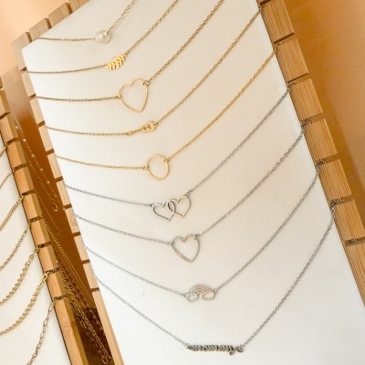 Conjunto de colares dourados e prateados com vários pingentes em suporte branco e madeira