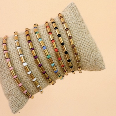 Conjunto de pulseiras coloridas com contas retangulares sobre almofada bege.