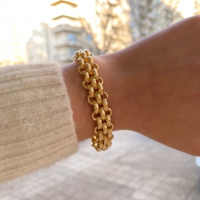 Pulseira dourada de elos entrelaçados no pulso sobre camisola bege