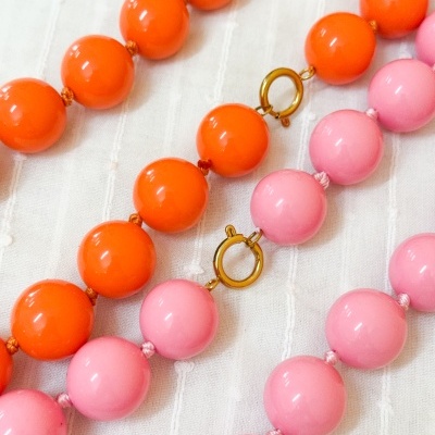 Colares de contas grandes laranja e rosa com fechos dourados sobre tecido branco