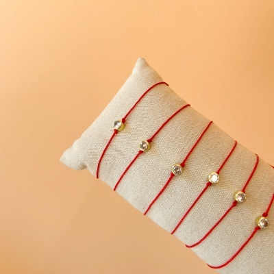 Pulseiras de fio vermelho com pendentes dourados sobre almofada bege