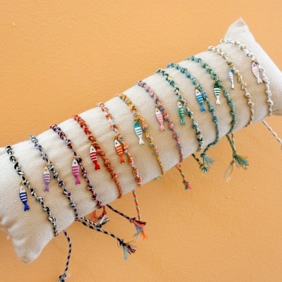 Pulseiras trançadas coloridas com pendentes de peixe expostas num suporte de tecido