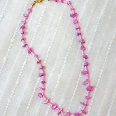 Colar de contas cor-de-rosa com pedras magentas sobre tecido branco