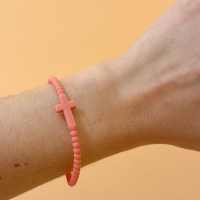 Pulsera rosa com cruz no pulso sobre fundo laranja claro
