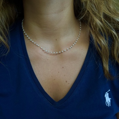 Colar de pérolas em pescoço com camisola azul com bordado branco