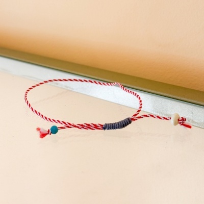 Pulseira de cordão vermelho e branco com contas azul e branca sobre superfície bege
