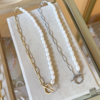 Colares com pérolas e elos metálicos sobre suporte de veludo bege.