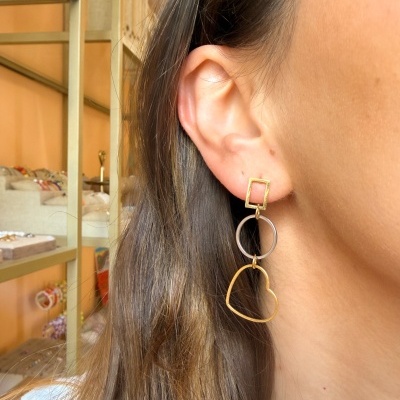 Brincos geométricos dourado e prata numa orelha feminina com cabelo castanho