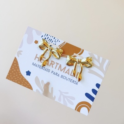 Cartão com pendentes dourados em forma de laço e texto HEARTMATE MATERIAIS PARA BIJUTERIA