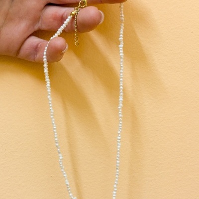 Colar de pérolas brancas com fecho dourado segurado por uma mão